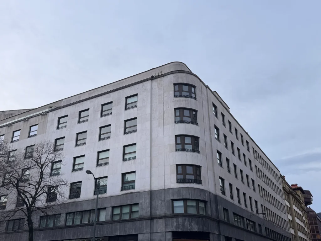 Edificio de oficinas de piedra clara con esquina curva y ventanas regulares en Bilbao
